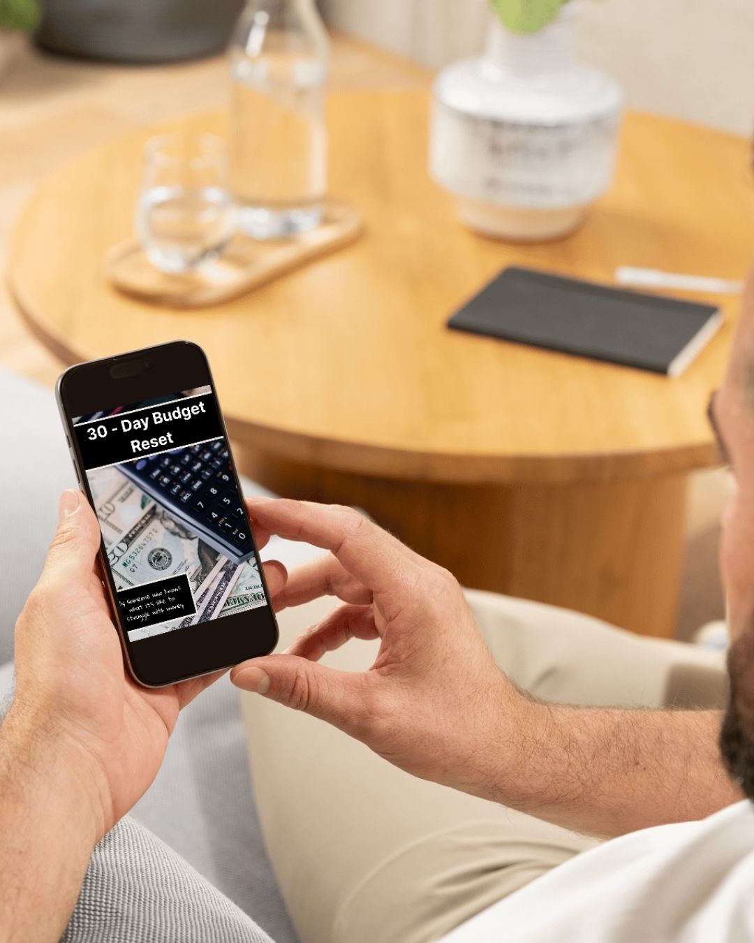 Person holding a smartphone with a budget app displayed, sitting in a casual setting.